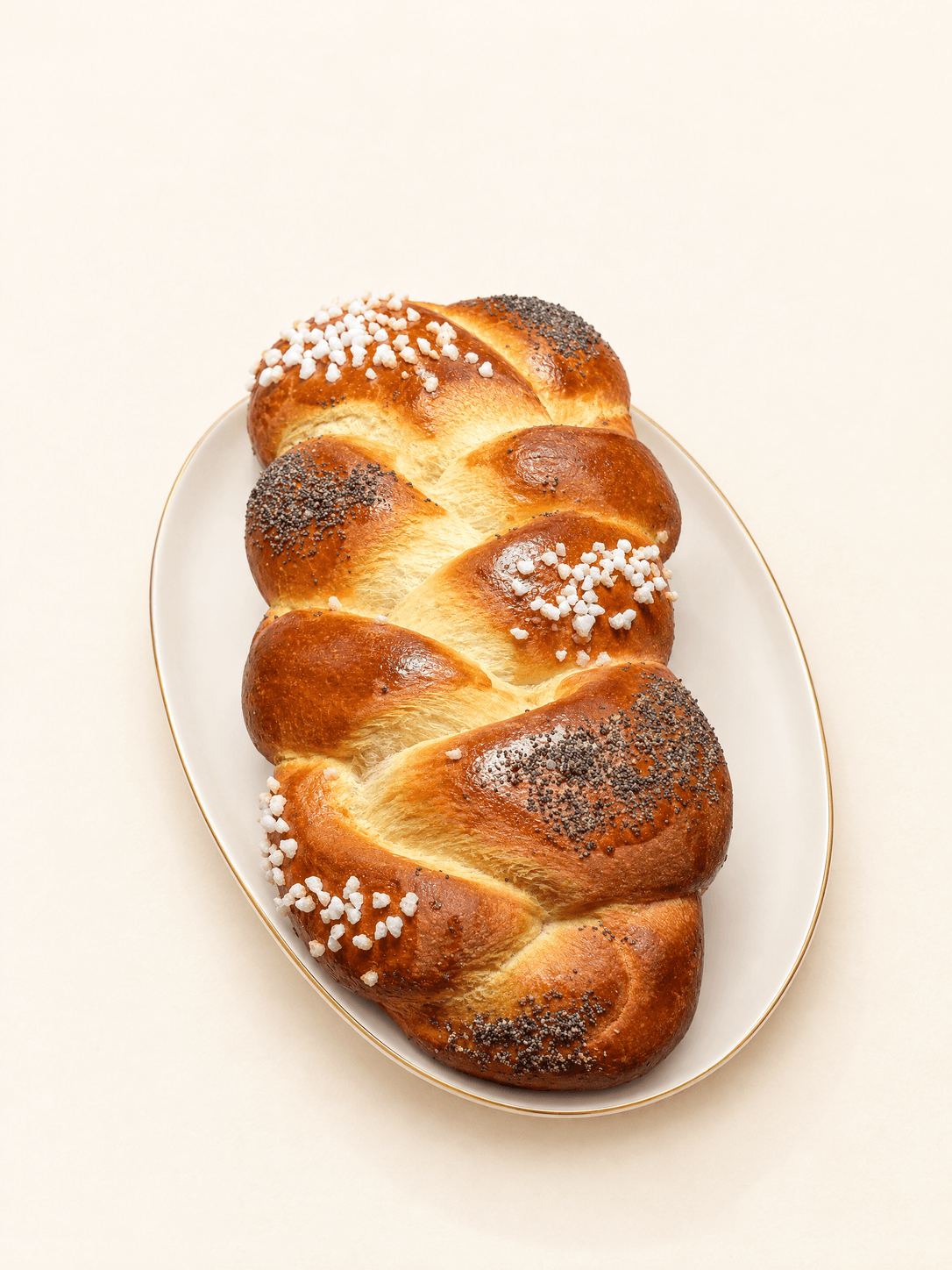 Braided brioche with pearl sugar and poppy seed on an ivory gold-rimmed platter